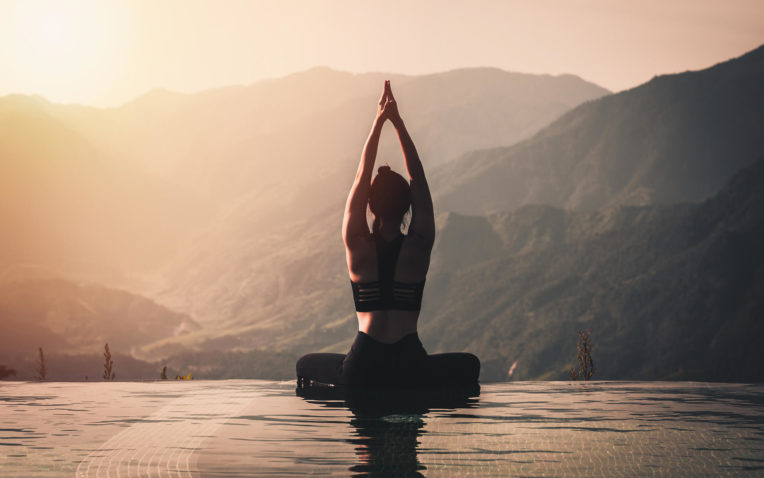 mulher pratica yoga, uma das terapias da ayurveda, acima do pico da montanha de manhã em frente a bela da natureza