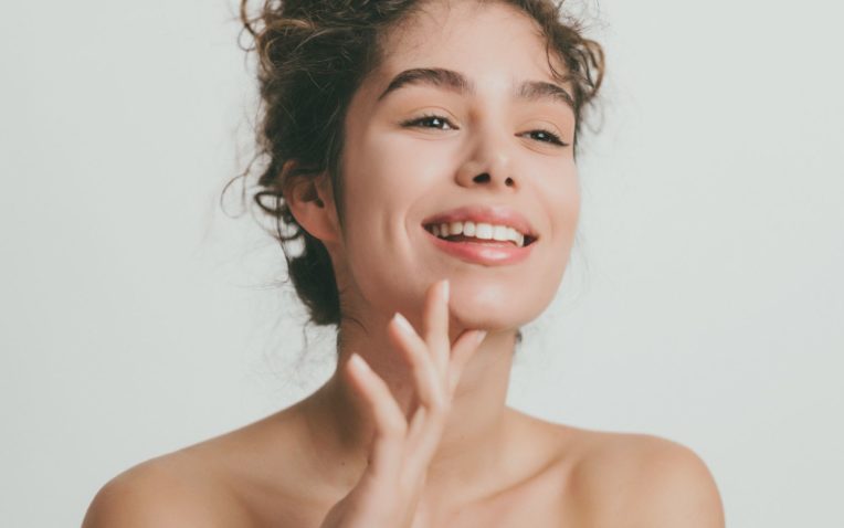 Rosto de mulher sorrindo, com a pele radiante e bem cuidada, indicando o uso de vitaminas para a pele.
