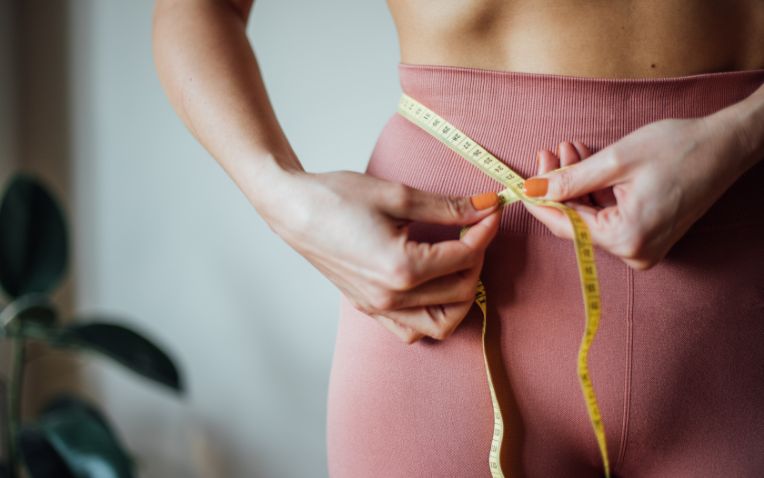 Mulher usa fita métrica para medir a circunferência abdominal e controlar o emagrecimento.