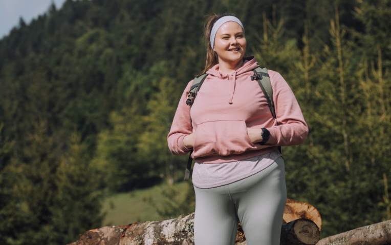 Mulher com lipedema vestindo casaco rosa e calça cinza.