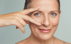 Mulher de olhos azuis com a mão no rosto, expressando uma sensação de contemplação ou reflexão.