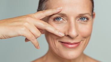 Mulher de olhos azuis com a mão no rosto, expressando uma sensação de contemplação ou reflexão.
