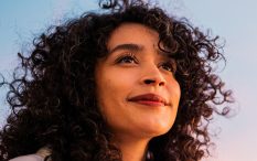 Mulher de cabelo cacheado olhando para o céu, com expressão de admiração e curiosidade.